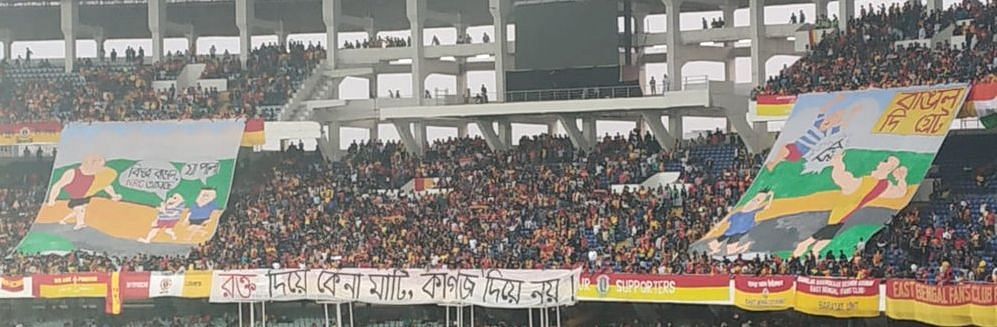 A banner  by East Bengal fans read Rokto Diye Kena Maati, Kaagoj Diye Noi (Land bought with blood, not with papers)