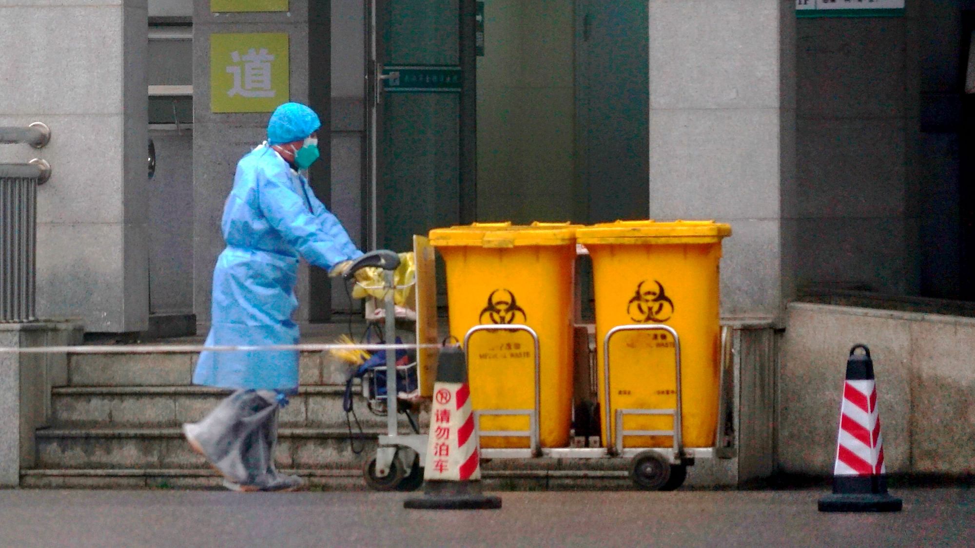 Staff move bio-waste containers past the entrance of the Wuhan Medical Treatment Center, where some infected with a new virus are being treated on Wednesday, 22 January.
