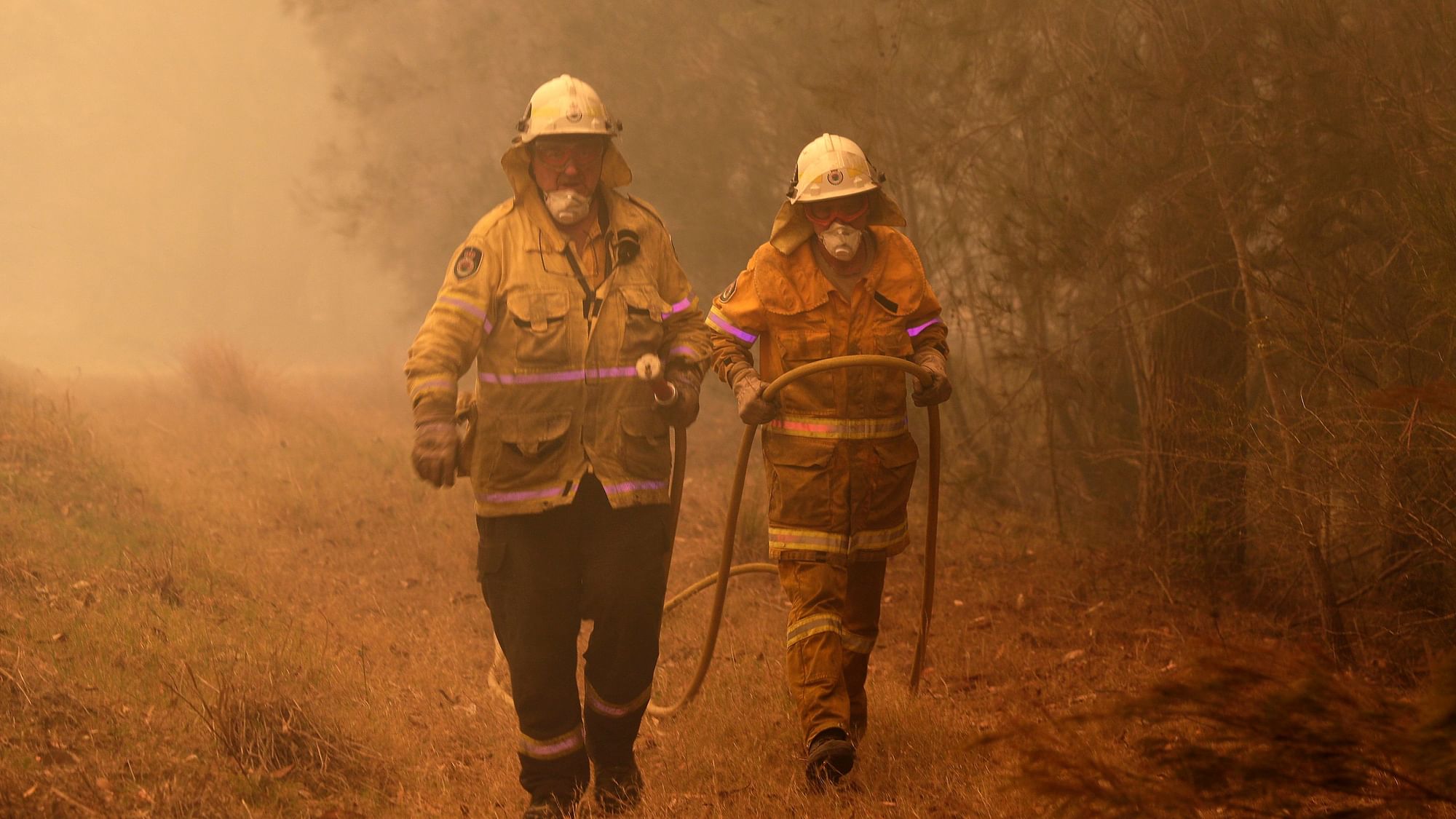 Firefighters drag their water hose after putting out a spot fire near Moruya, Australia.&nbsp;