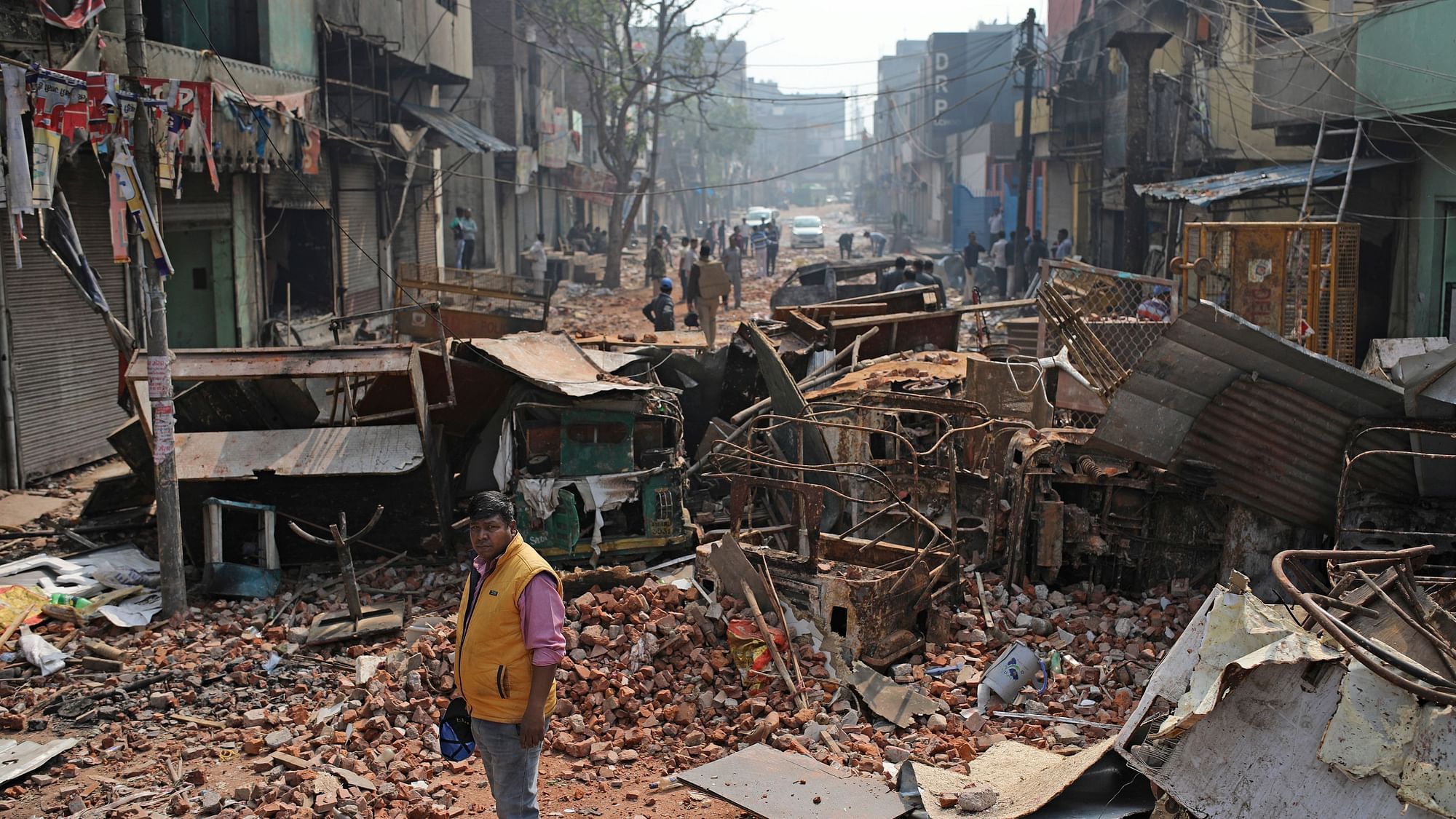 A Delhi municipal worker stands next to the remains of vehicles, and other materials on a street vandalised in violence in New Delhi, on  27 February.
