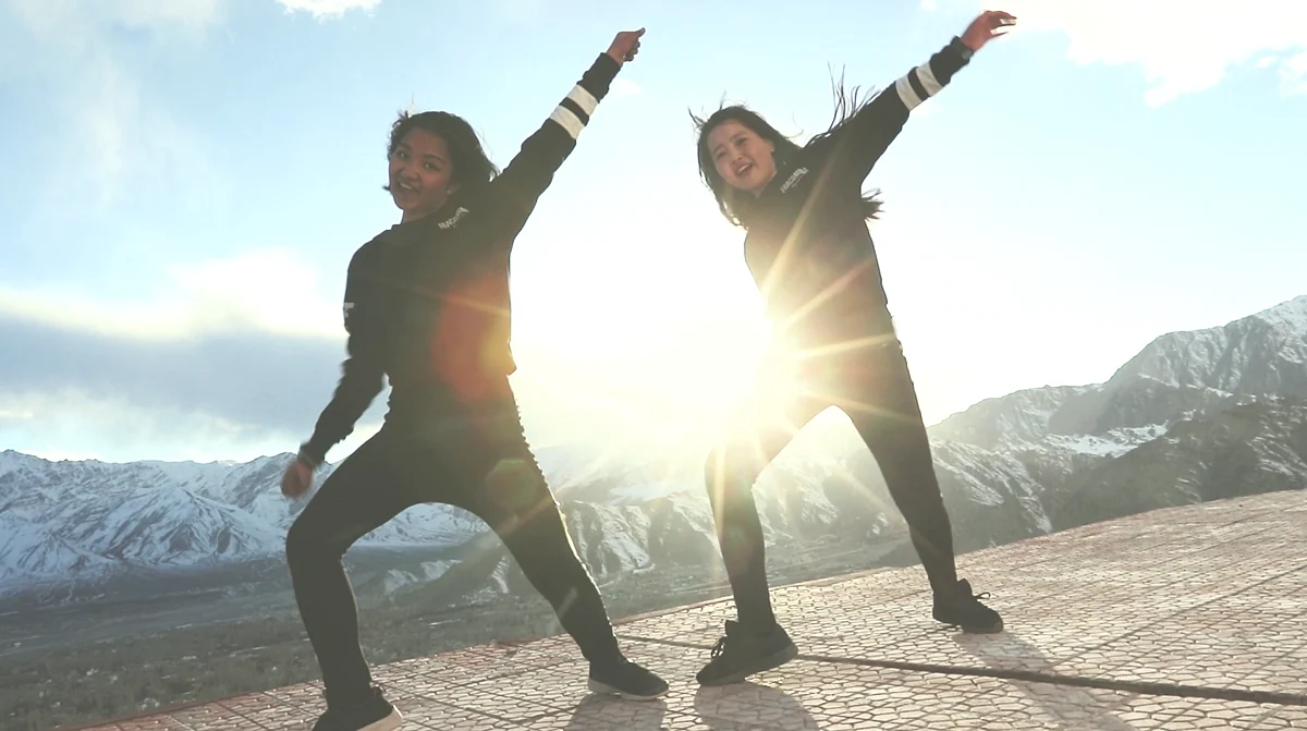 Two girls dance in the backdrop of snow-capped mountains.