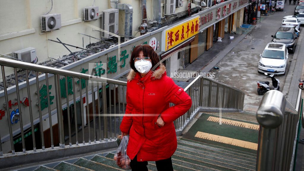 A woman wearing a protective face mask walks past closed restaurants following the coronavirus outbreak in Beijing, Monday, 2 March 2020.