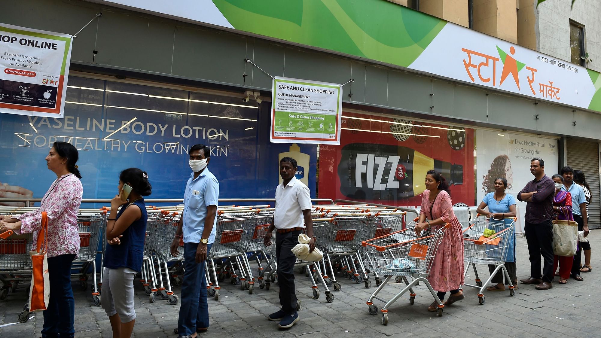 People wearing face masks in the wake of coronavirus pandemic stand in queue to buy groceries, at Churchgate in Mumbai, Saturday, 21 March  2020.&nbsp;