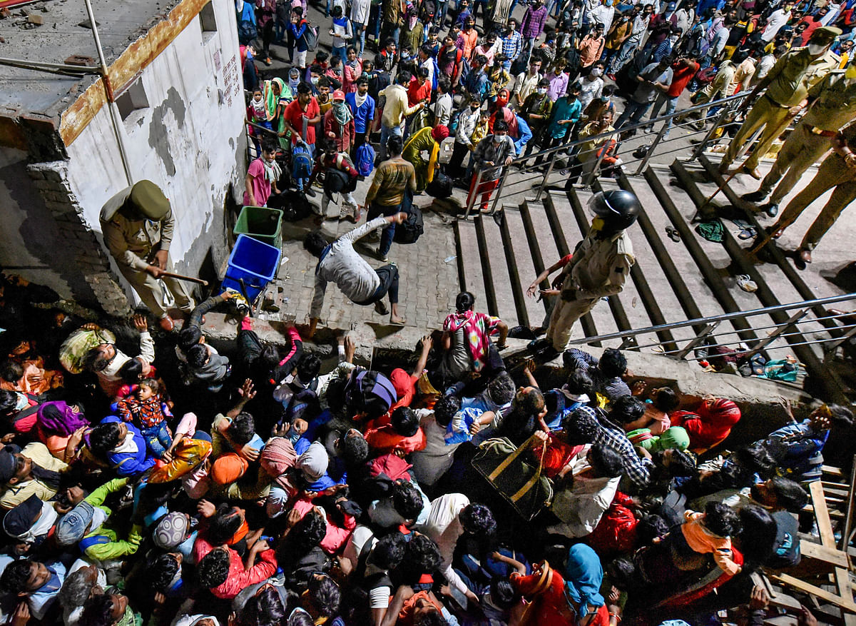 Policemen try to regulate as migrants try to cross a boundary wall in an attempt to board a bus to their native villages during a nationwide lockdown, imposed in the wake of coronavirus pandemic at Kaushambi, in Ghaziabad, Saturday, March 28, 2020.