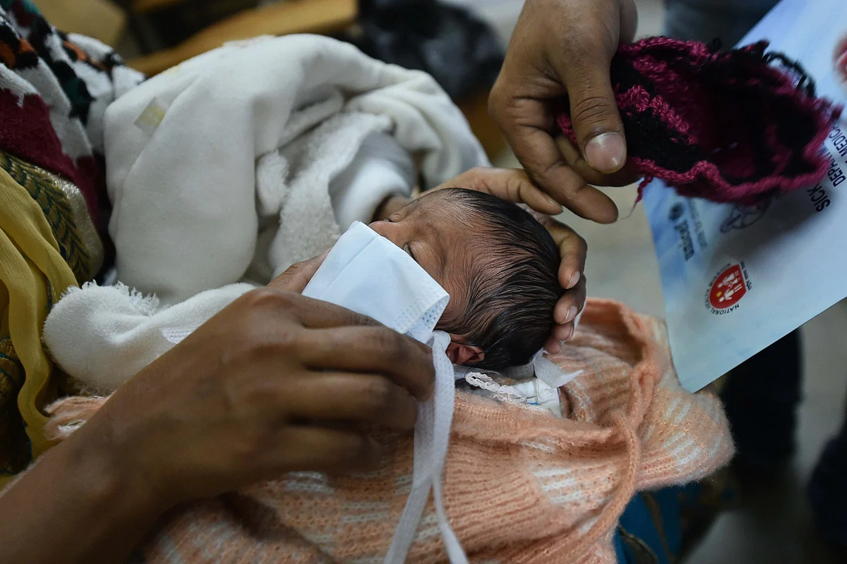 A family member puts a protective mask on a new-born baby in the wake of coronavirus pandemic, before being weighed at Hailate Hospital, in Kanpur, Friday, 20 March 2020.