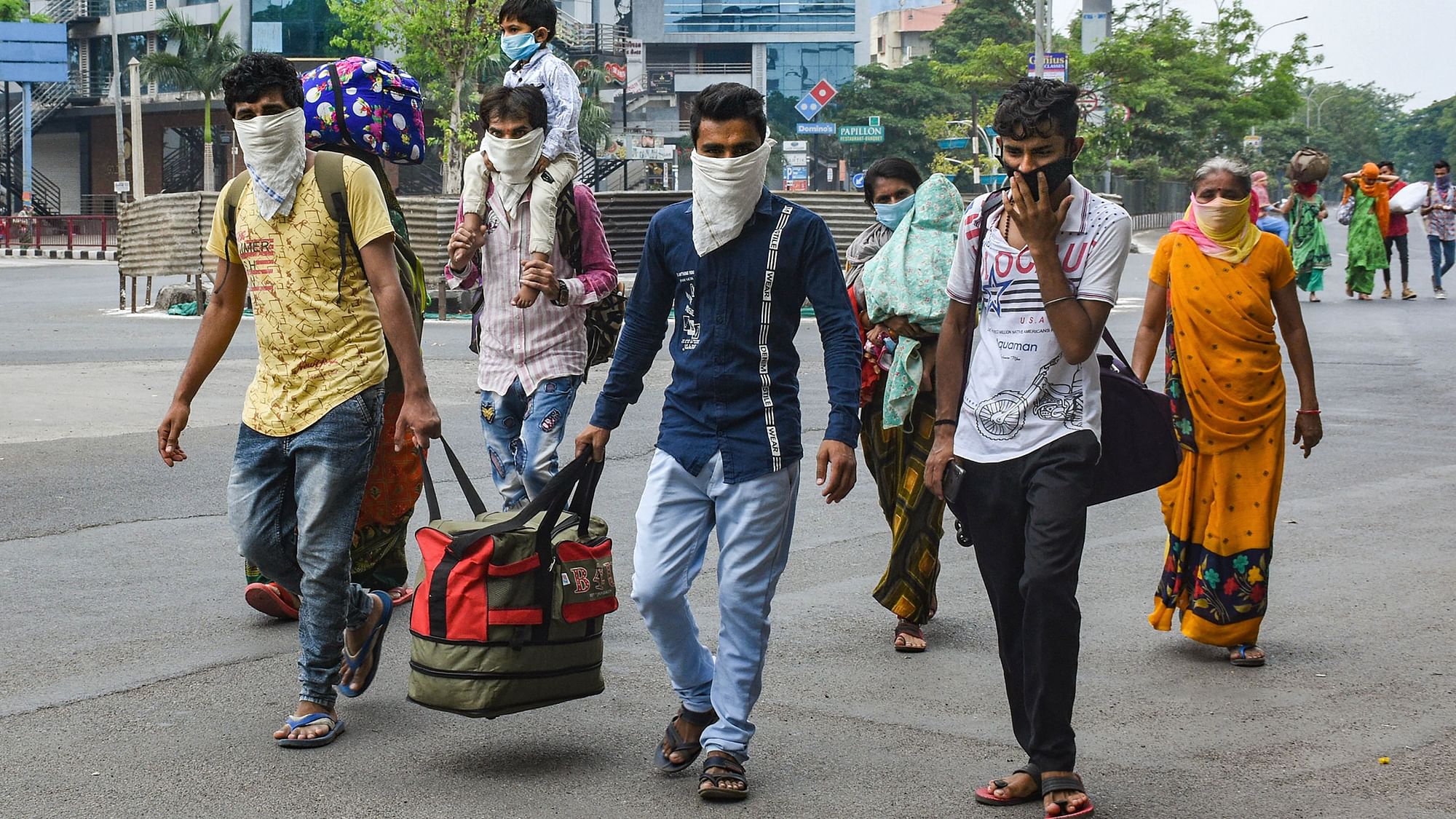 Migrant labourers along with their families walk on a road after they couldn’t find any transport vehicle to return to their native places, during the complete lockdown to contain the coronavirus spread, in Surat, Thursday, 26 March.