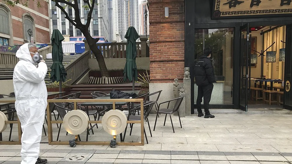 A store worker in protective suit waits for customers at a re-opened retail street in Wuhan in central China's Hubei province on Monday, March 30, 2020.