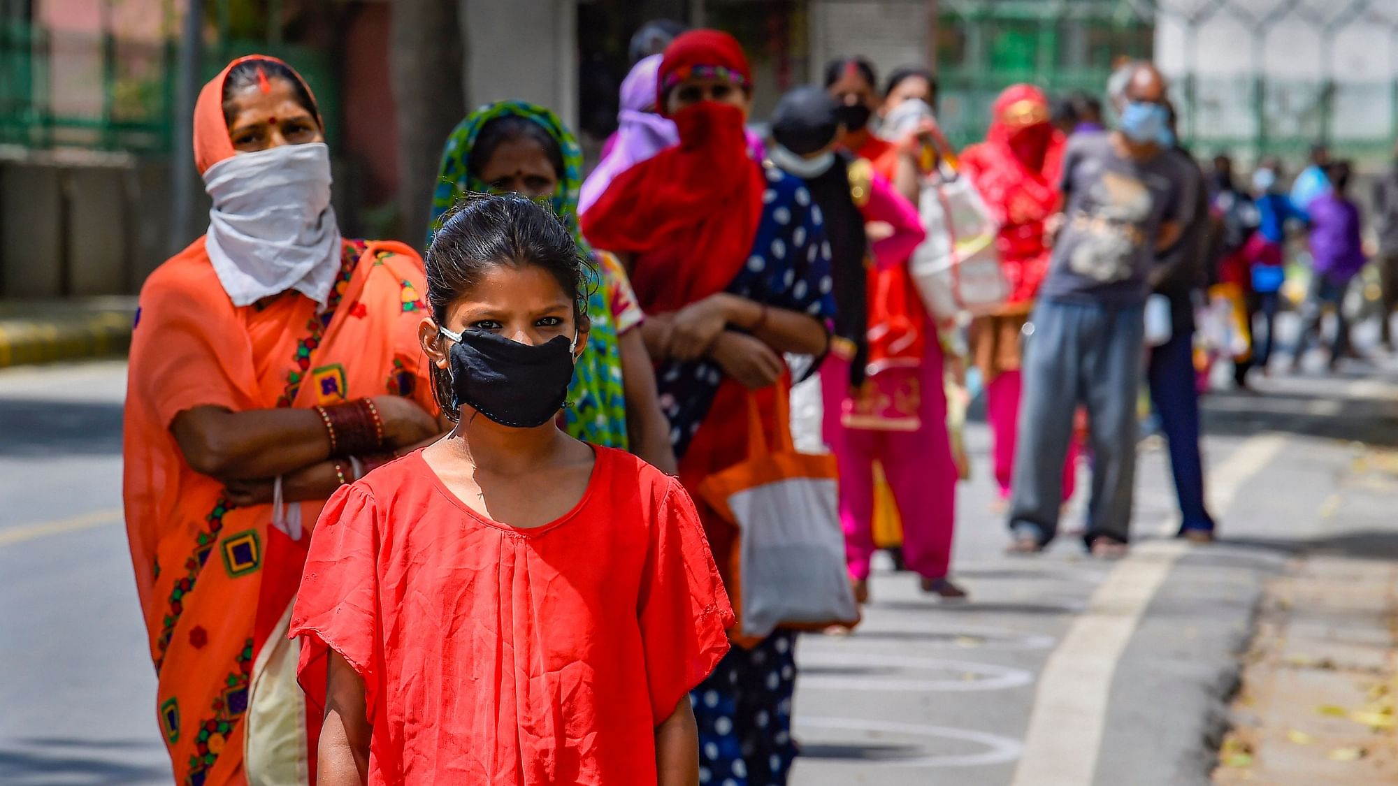 People wearing masks stand in a queue to collect food distributed by Delhi government volunteers, Monday.