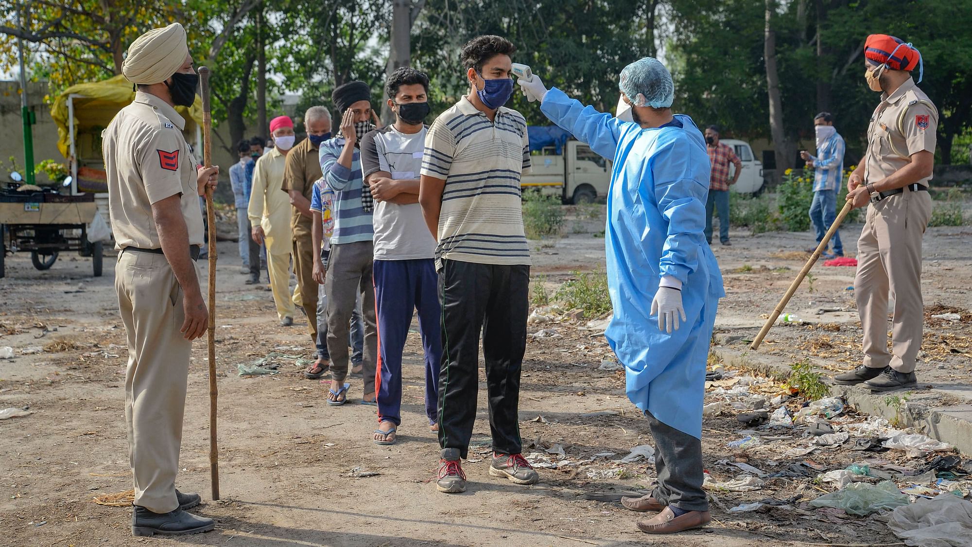 A health worker wearing a protective suit uses a thermal screening device on vendors during a government-imposed nationwide lockdown as a preventive measure against the spread of coronavirus, in Jalandhar, Tuesday,14 April 2020.