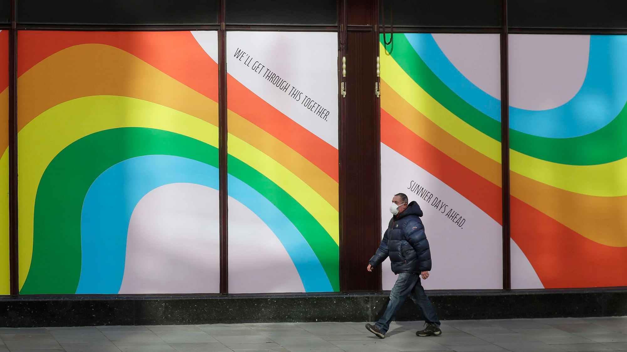 A man wearing a face mask to protect against catching the coronavirus walks past a window display of rainbows in the windows of the famous London department store Harrods in London, Tuesday, 31 March, 2020.&nbsp;