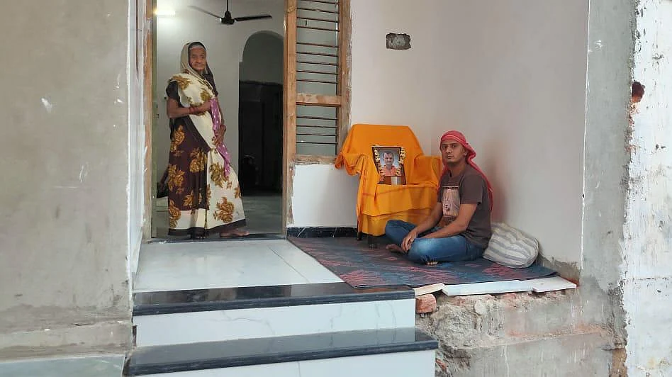 This is Ramesh’s home, his son Rahul is sitting outside with his father’s picture mounted on a chair. As is custom, he has shaved his head.