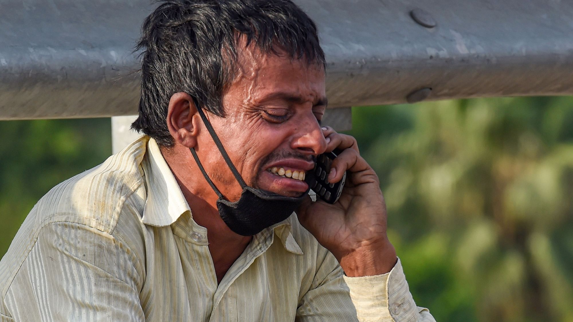 A migrant labourer reacts while talking to a relative over his mobile phone, at Nizamuddin Bridge in New Delhi, Monday.