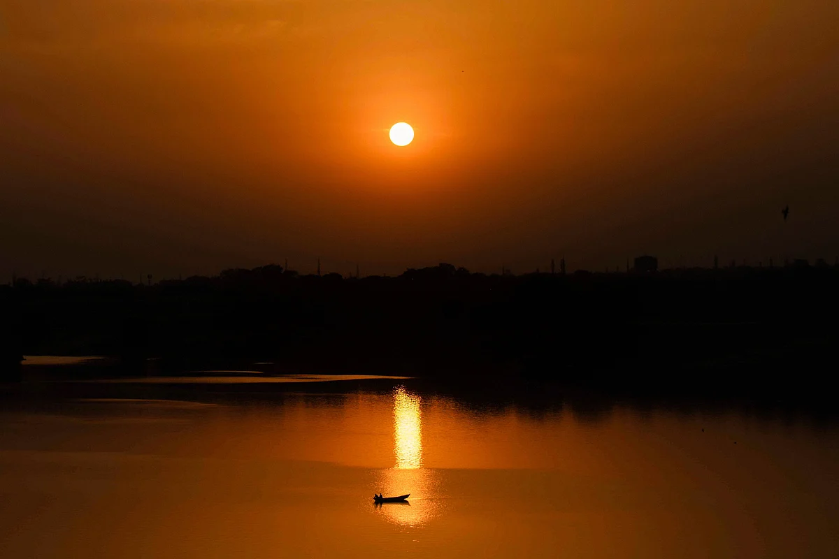 A boat is silhouetted against the setting sun as it travels across a river, in Prayagraj on Monday.