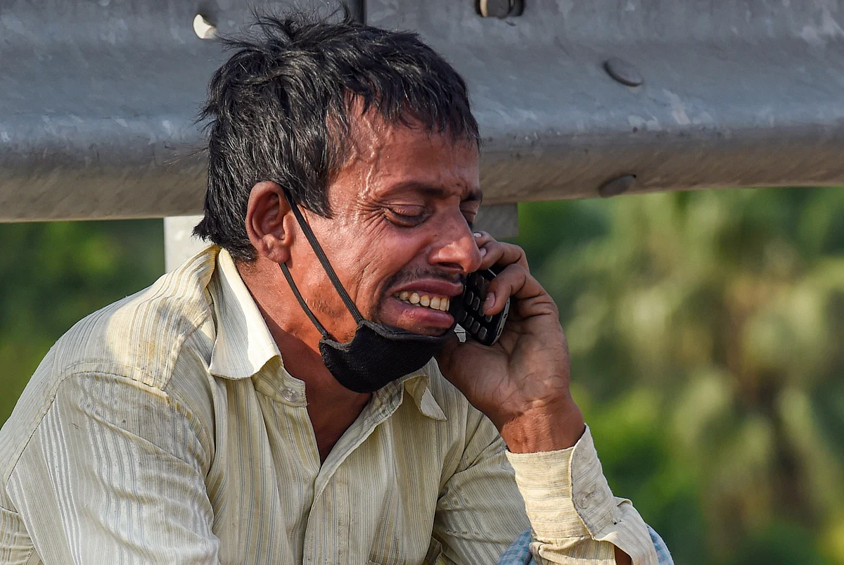 A migrant labourer reacts while talking to a relative over his mobile phone, at Nizamuddin Bridge in New Delhi, Monday.