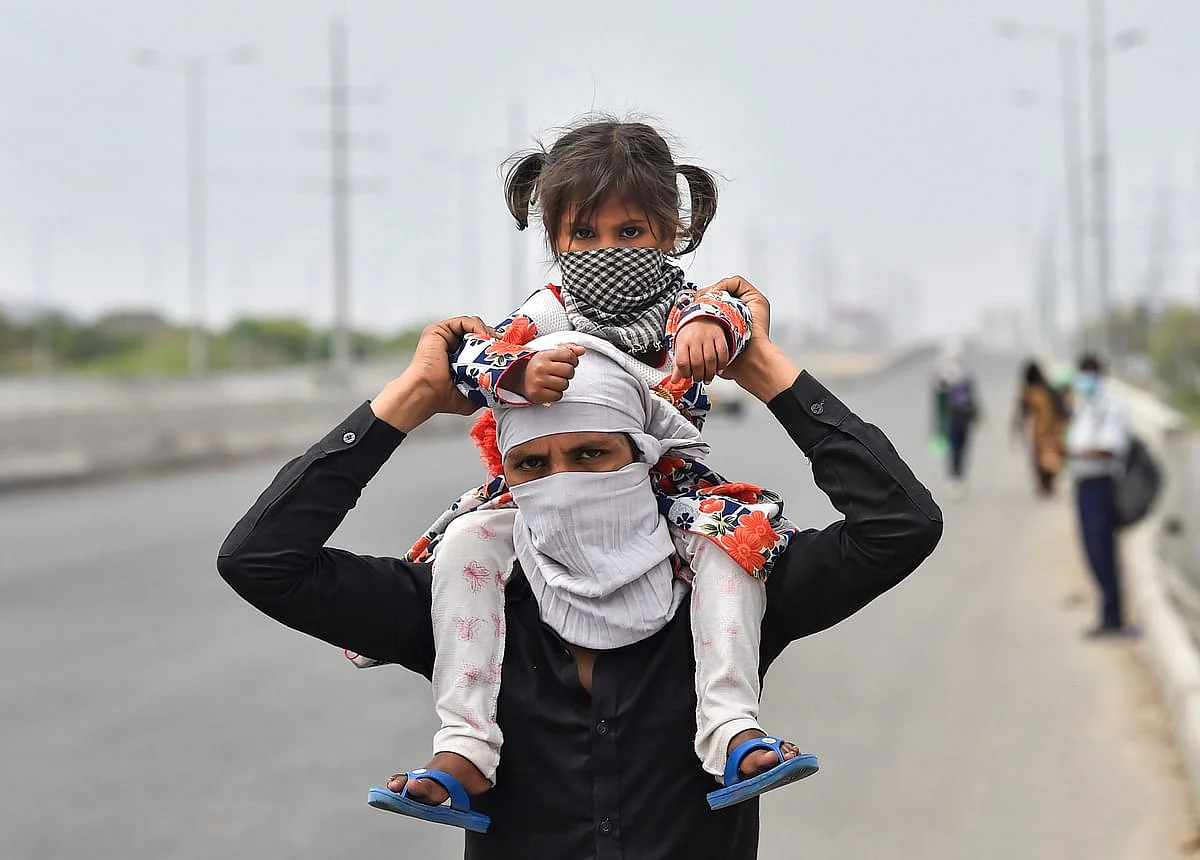 A worker with a child on his shoulder walks to his village amid a nationwide complete lockdown, on the NH24 near Delhi-UP Border in Ghaziabad, Thursday, 26 March 2020.