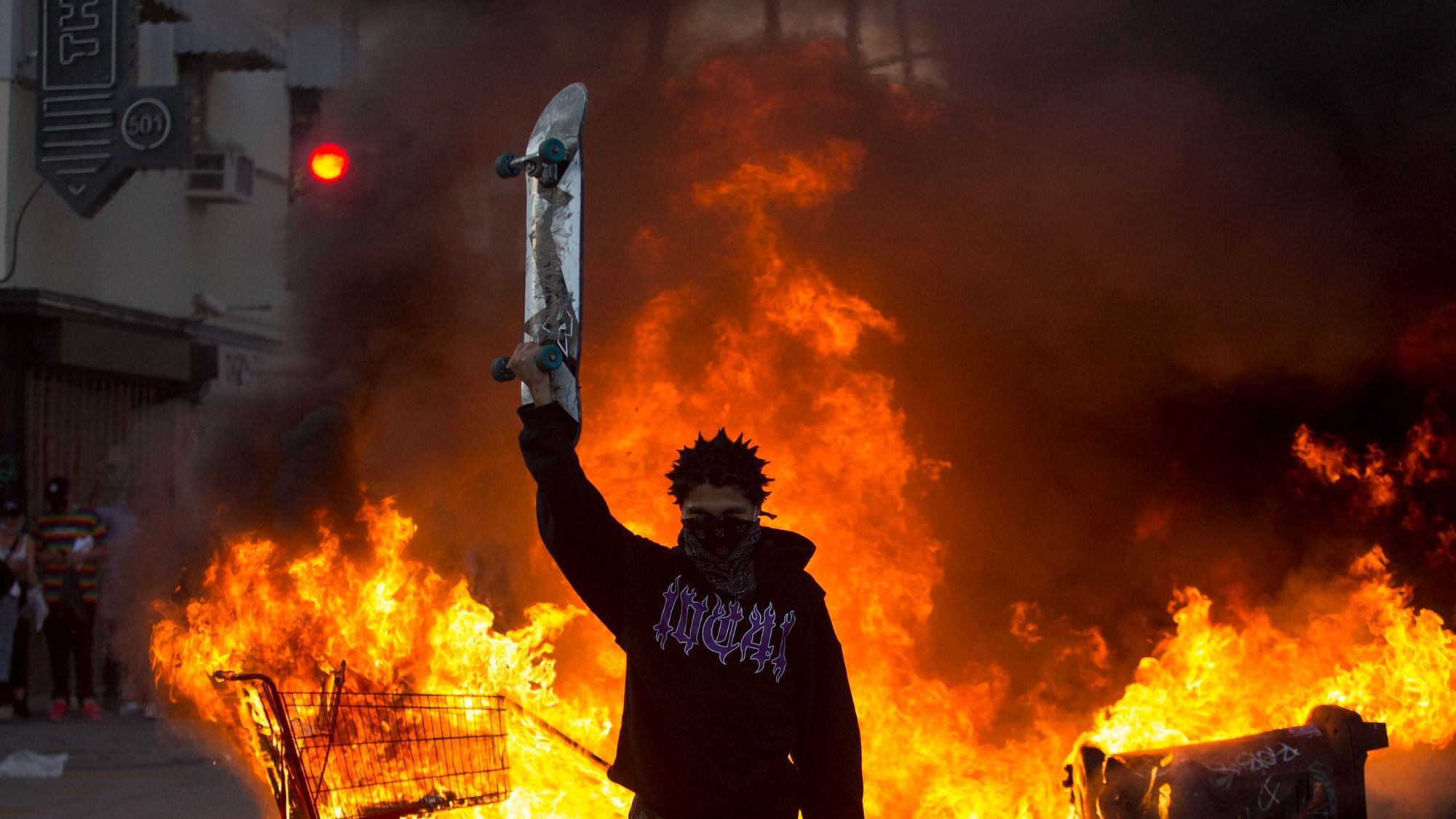 A protester holds a skateboard in front of a fire in Los Angeles, Saturday, 30 May 2020, during a protest over the death of George Floyd, a handcuffed black man who died in Minneapolis police custody on 25 May.