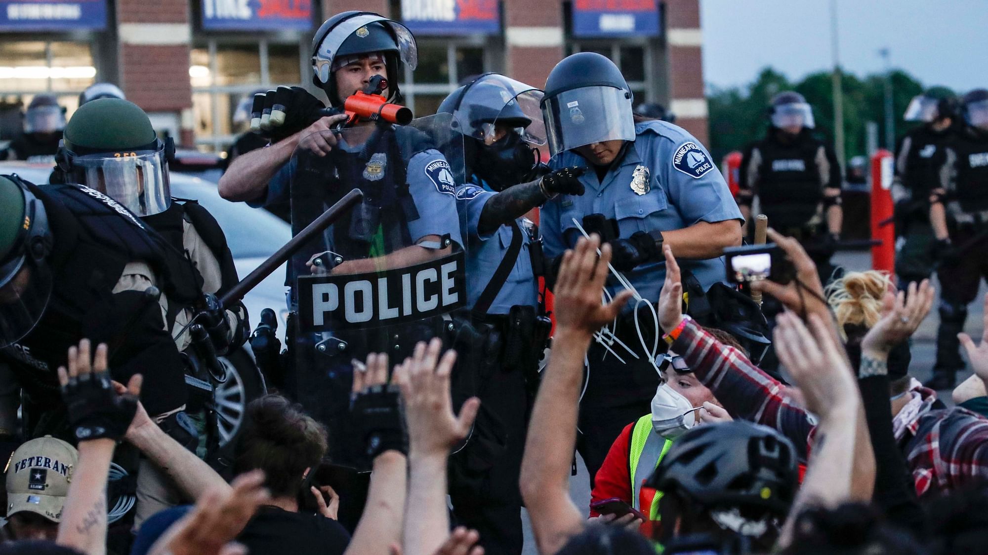A police officer points a hand cannon at protesters who have been detained pending arrest on South Washington Street, Sunday, 31 May, in Minneapolis. Protests continued following the death of George Floyd, who died after being restrained by Minneapolis police officers on Memorial Day.