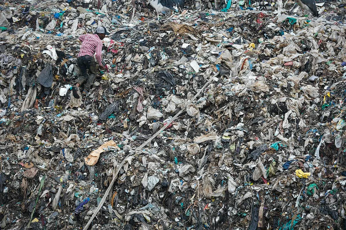 A man climbs a wall of garbage at a landfill in Kenya. <br>