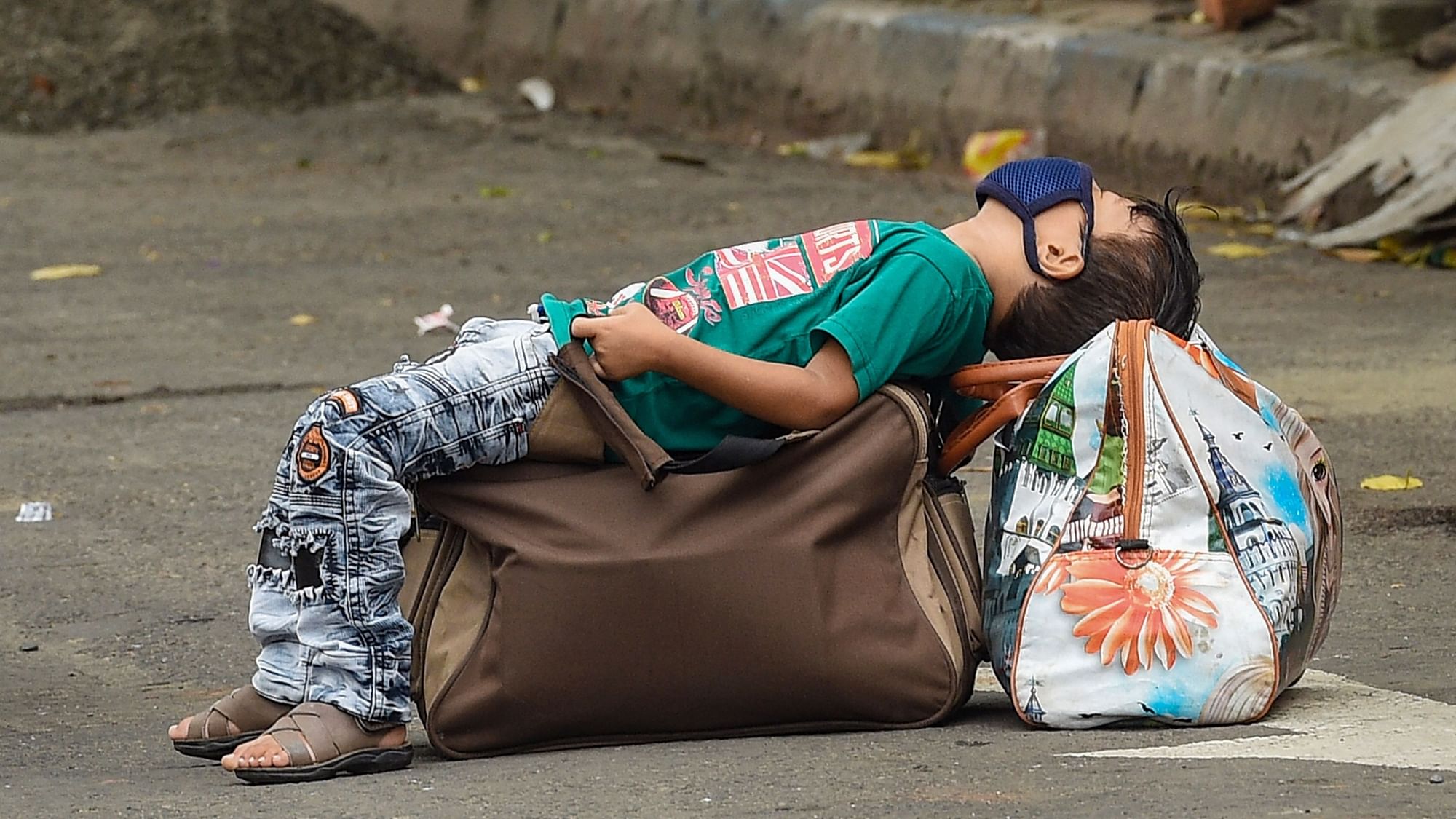 A boy takes rest on the luggage along a road, during Unlock 2.0, in Kolkata.
