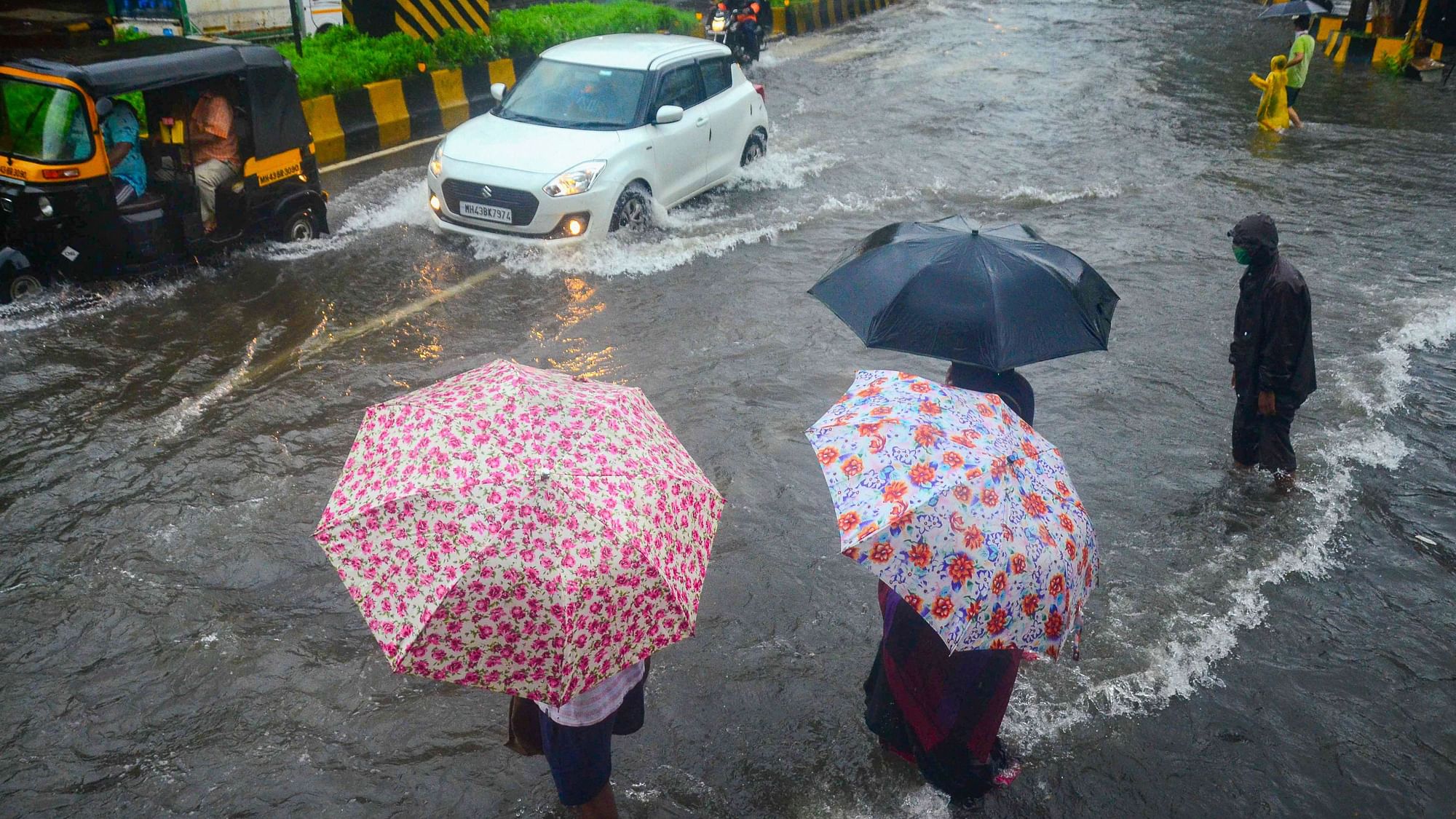 Commuters wait to cross a waterlogged street as vehicles ply, during heavy rainfall, at Vashi in Navi Mumbai, Sunday, July 5, 2020.