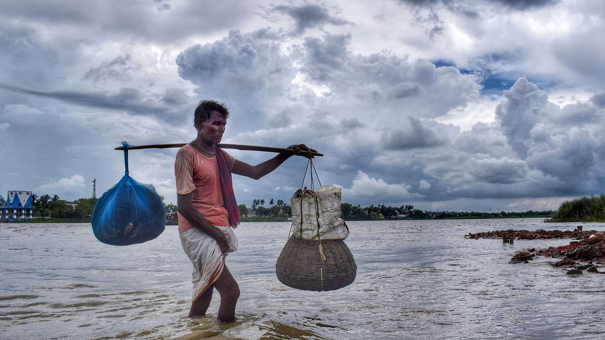 A man carrying his belongings walks at the banks of Hooghly river in the backdrop of dark clouds looming in the sky in Nadia district of West Bengal on Wednesday, 8 July.