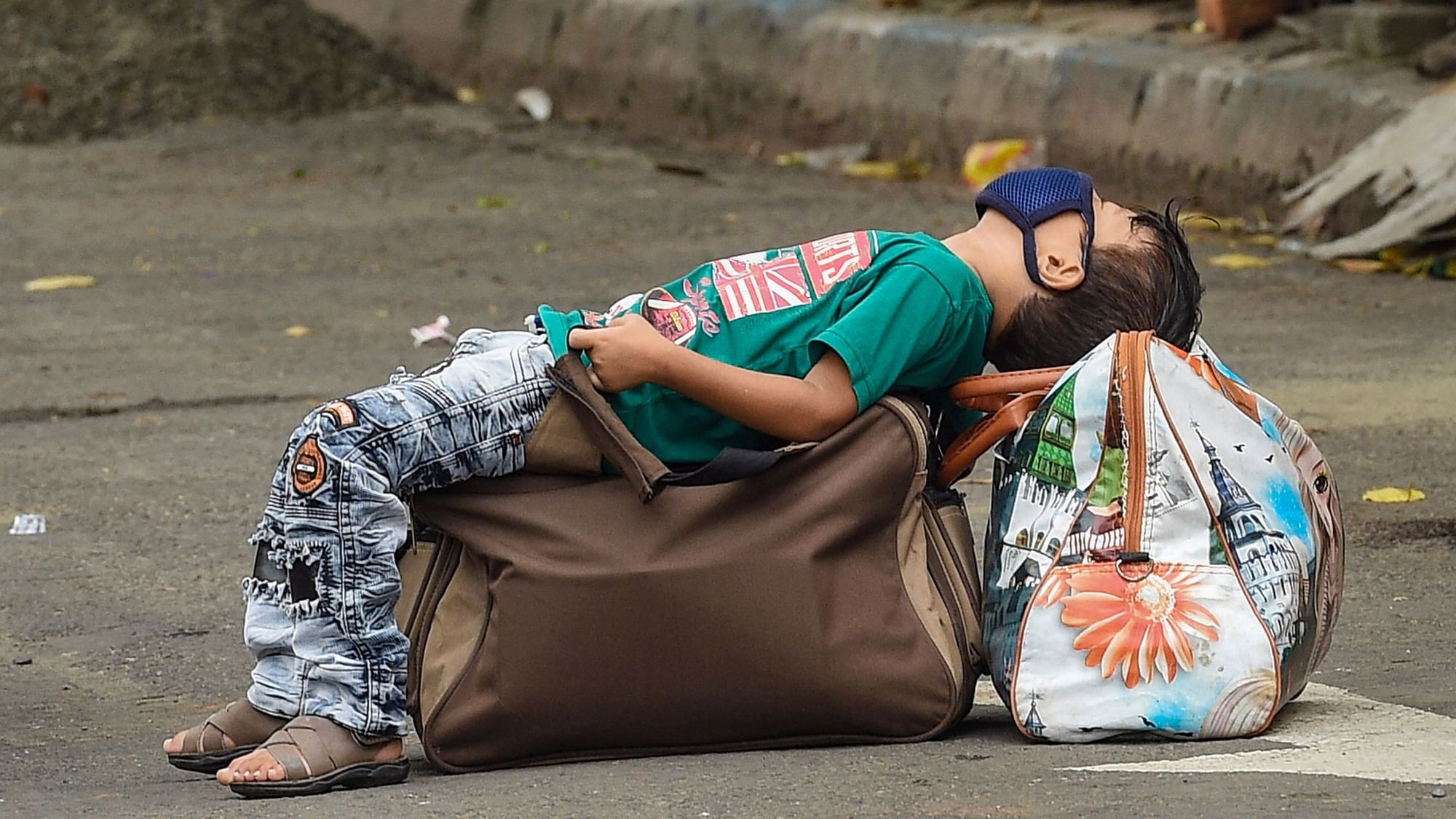 A boy takes rest on luggage along the road in Unlock 2.0 in Kolkata.&nbsp;