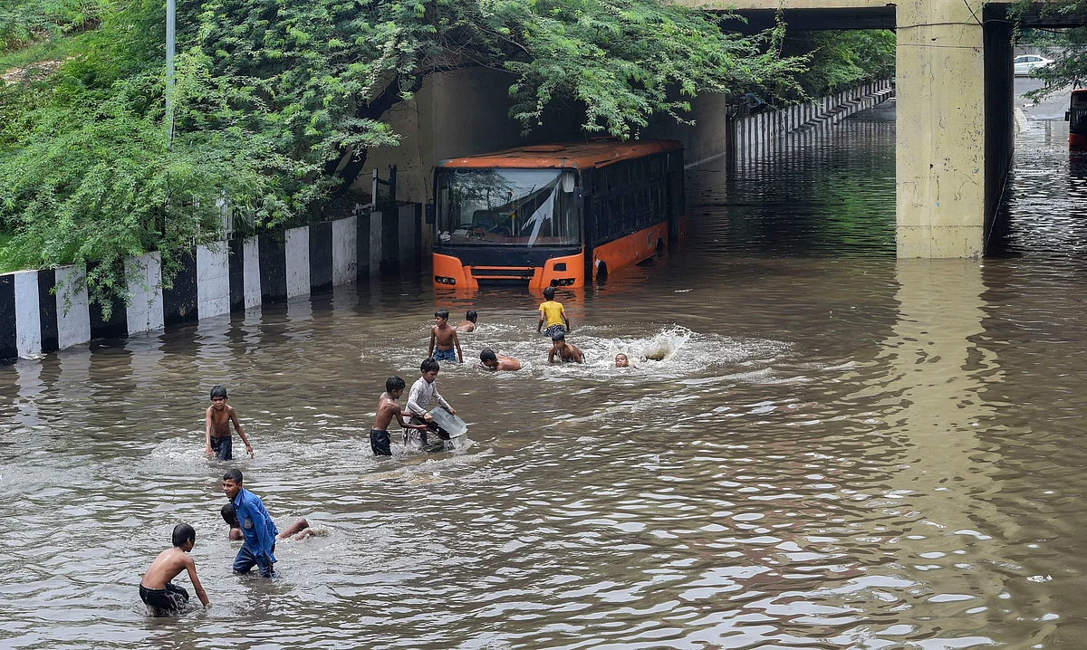 A DTC bus stuck at waterlogged Zakhira underpass as children play, after rains in New Delhi.
