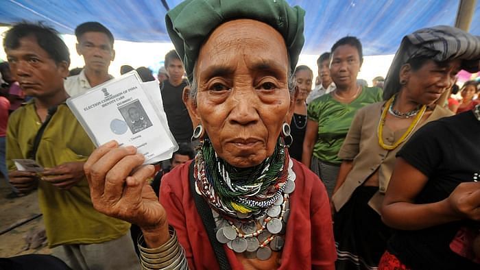 A Bru refugee wearing traditional ornaments displays her voting card as she and others wait to cast their ballots at Thamsapara relief camp in Tripura on April 1, 2014.