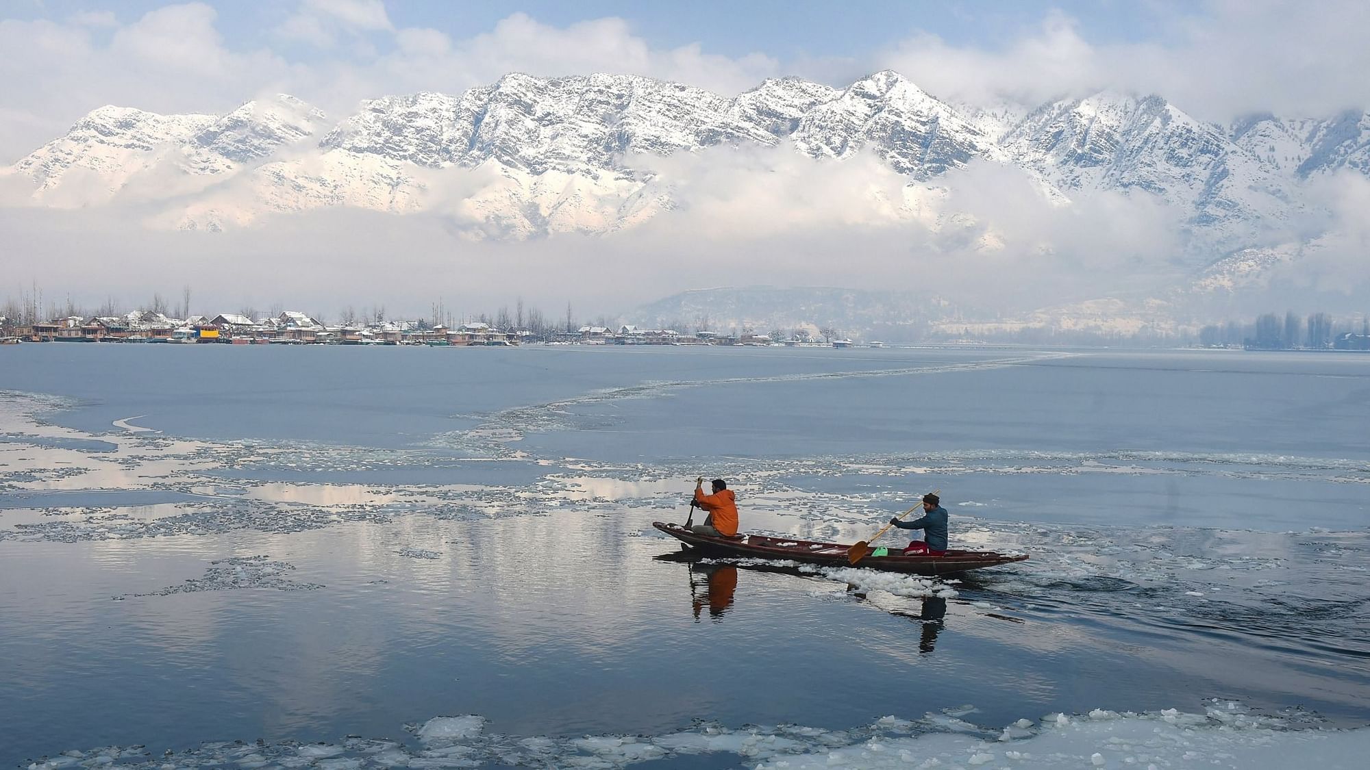 Srinagar: Boatmen row a boat across Dal Lake as snowclad Zabarwan mountains are seen in the backdrop after snowfall, in Srinagar, Wednesday, 6 January, 2021.&nbsp;