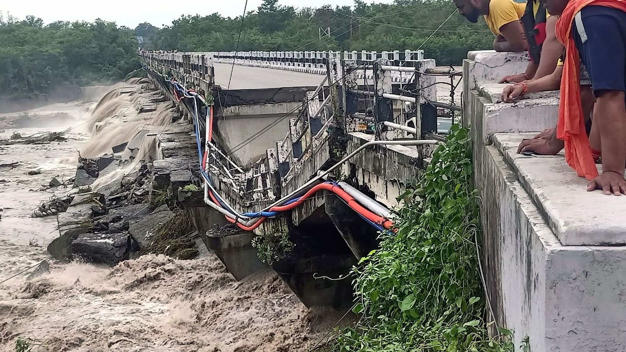 <div class="paragraphs"><p>Dehradun: People look at the Rani Pokhri bridge on the Dehradun Rishikesh highway that collapsed due to heavy rains, near Dehradun on Friday.</p></div>