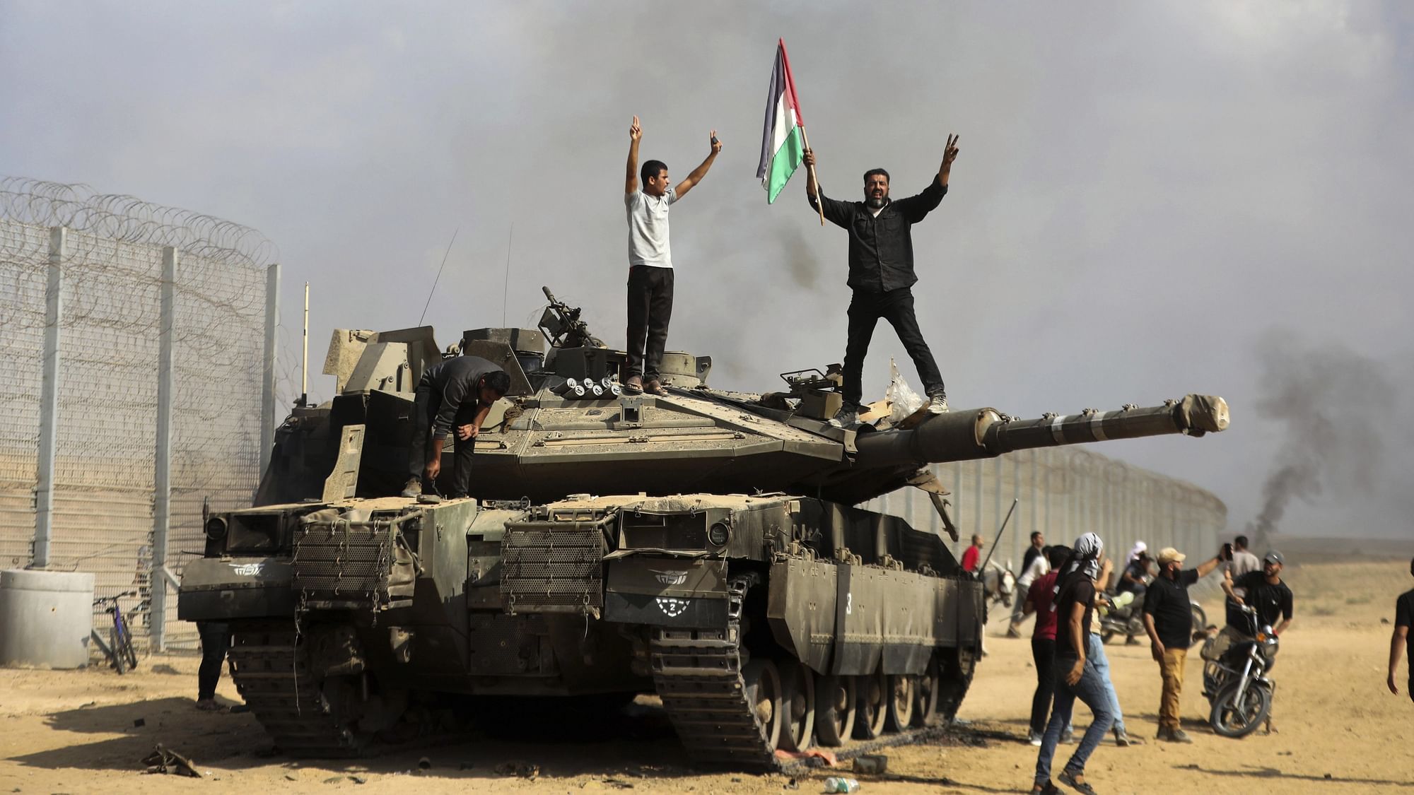 <div class="paragraphs"><p>Palestinians wave their national flag and celebrate by a destroyed Israeli tank at the Gaza Strip fence east of Khan Younis southern Saturday, Oct. 7, 2023. </p></div>