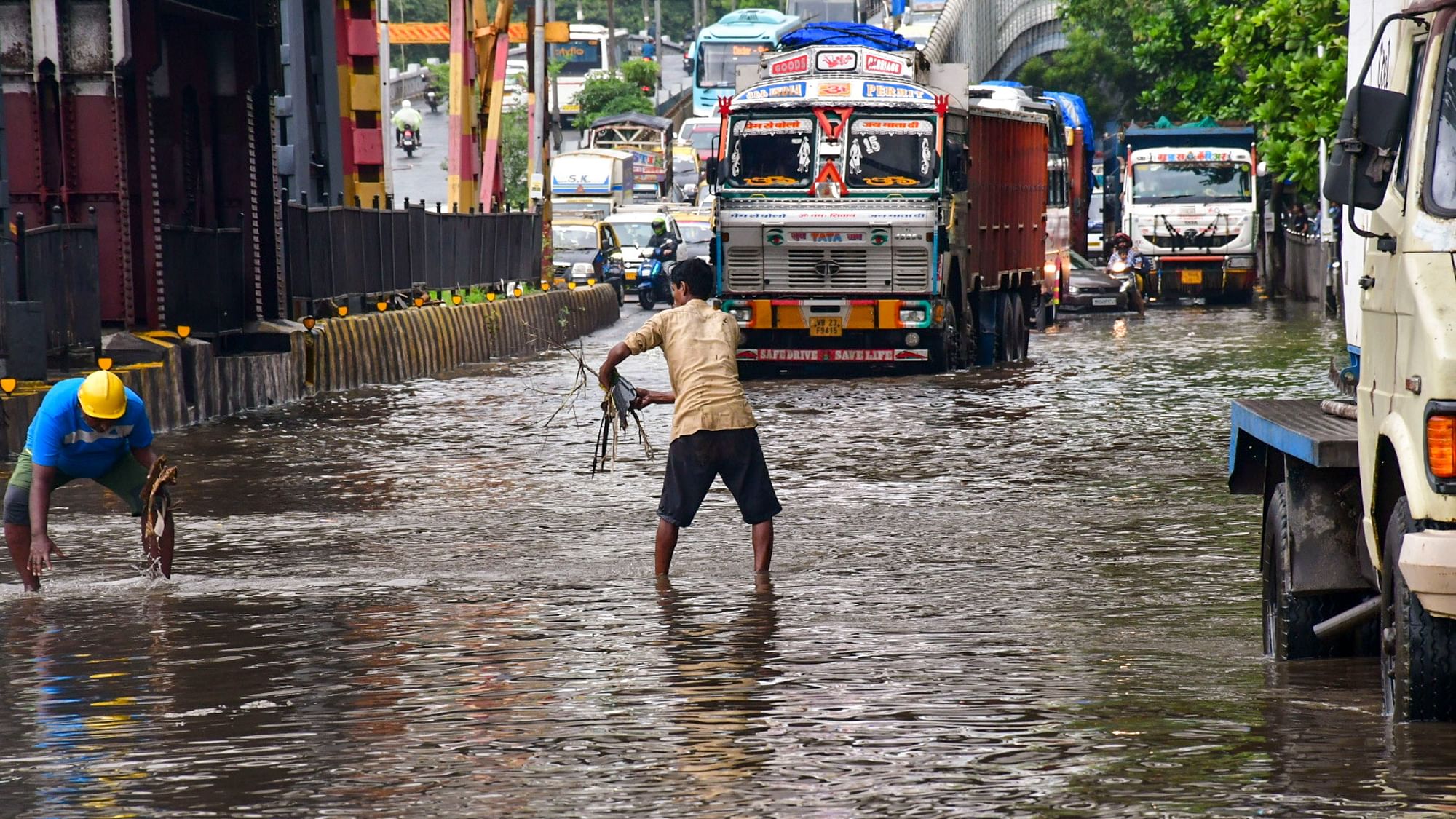 <div class="paragraphs"><p>Workers clear a waterlogged road in Mumbai as vehicles make their way following rains.</p></div>