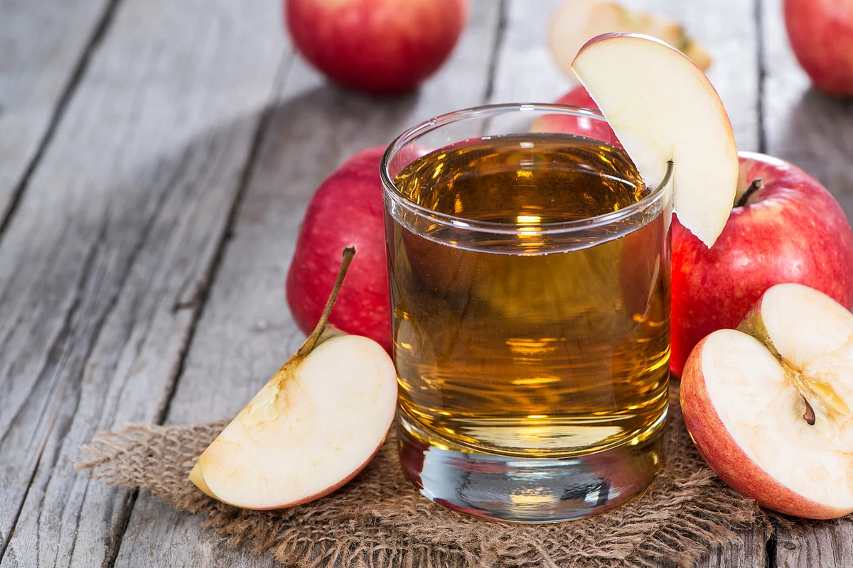 Glass of apple cider surrounded by freshly-cut apples. 