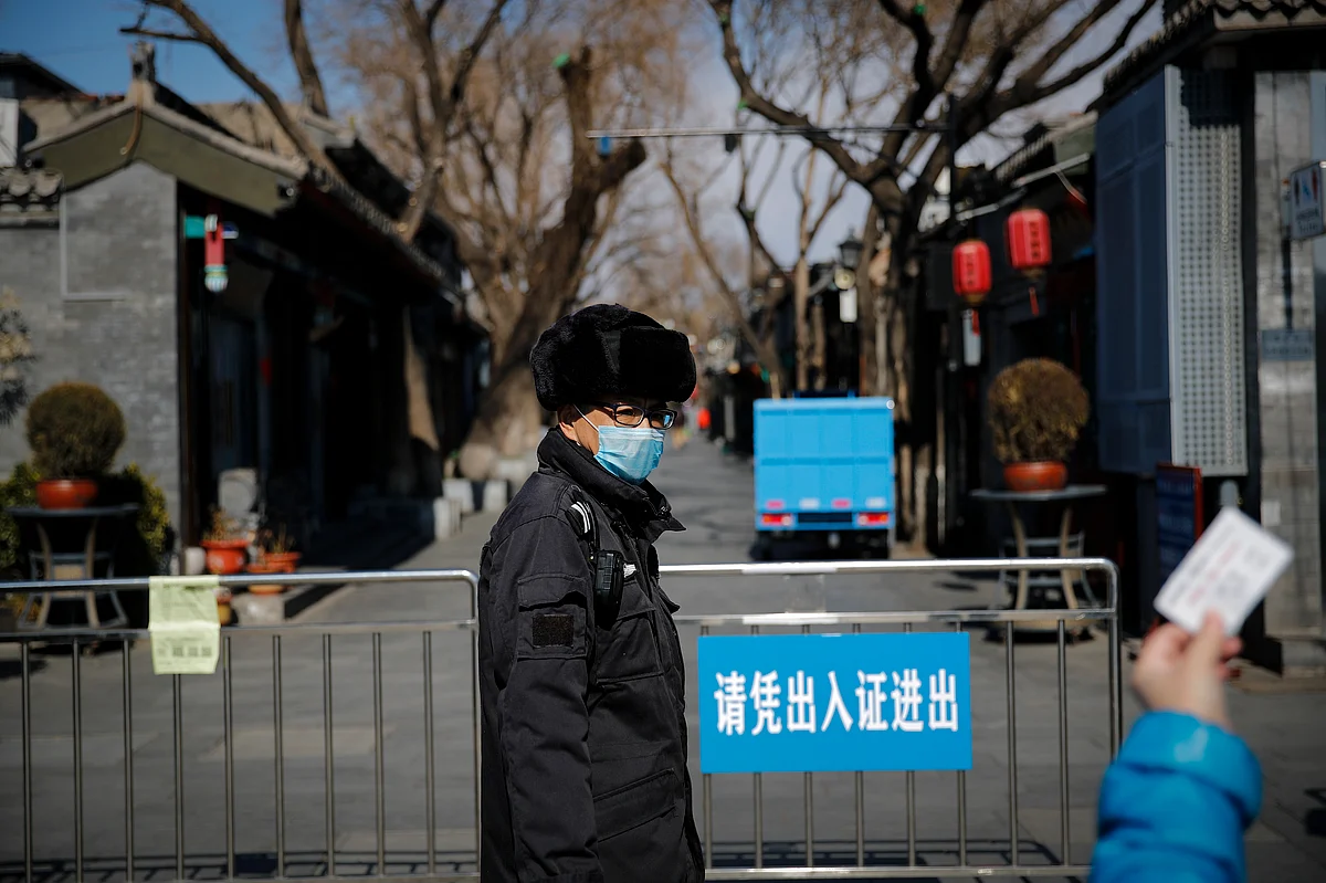 A masked security guard watches a resident showing her entry pass near a barricaded Nanluoguxiang, a popular tourist spot following the coronavirus outbreak in Beijing, Sunday, March 1, 2020.
