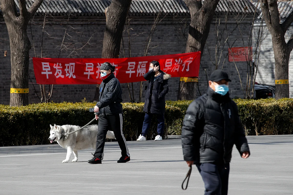 Residents wearing protective face masks walk by a propaganda banner which reads "Early detection, early reporting, early isolation and get early treatment" hangs on a neighborhood alley following the coronavirus outbreak in Beijing, Sunday, March 1, 2020.